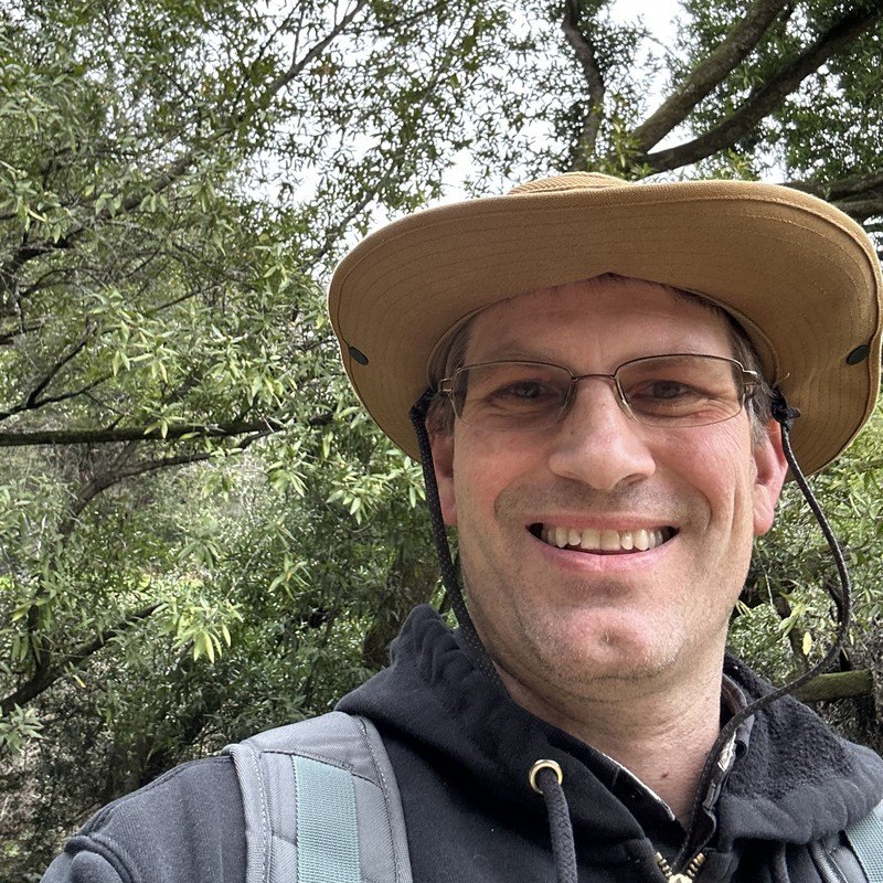 Michael Schuck, ISA Certified Arborist, in a field hat under a tree canopy
